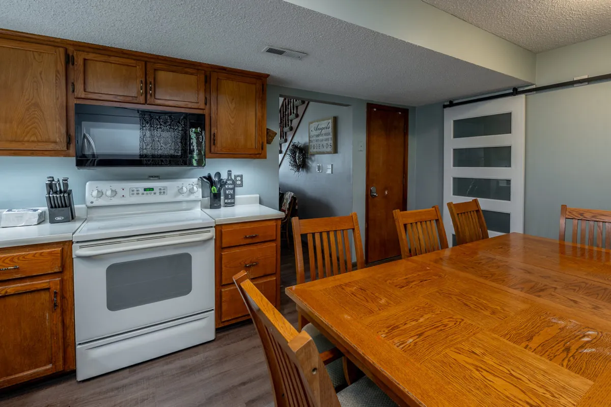 A view of the kitchen stove and adjacent dining table, surrounded by warm wooden cabinetry and decorative touches that enhance the inviting feel. The setup suggests space for cooking, sharing recipes, and gathering with friends or family.