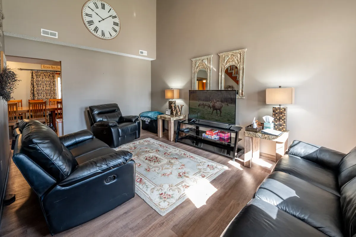 A cozy living area centered around black leather sofas, a decorative mirror, television, and a soft area rug, setting the stage for evenings spent watching TV, socializing, or enjoying game nights with friends and family.