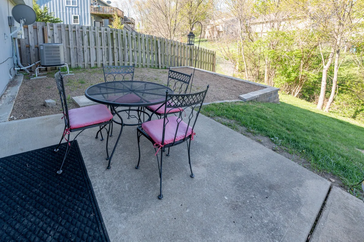 An inviting backyard scene featuring a round table with four chairs set on a green lawn, bordered by a wooden fence. The setup suggests outdoor dining or relaxing with friends, with ample space for activities like reading, conversation, or enjoying the fresh air.