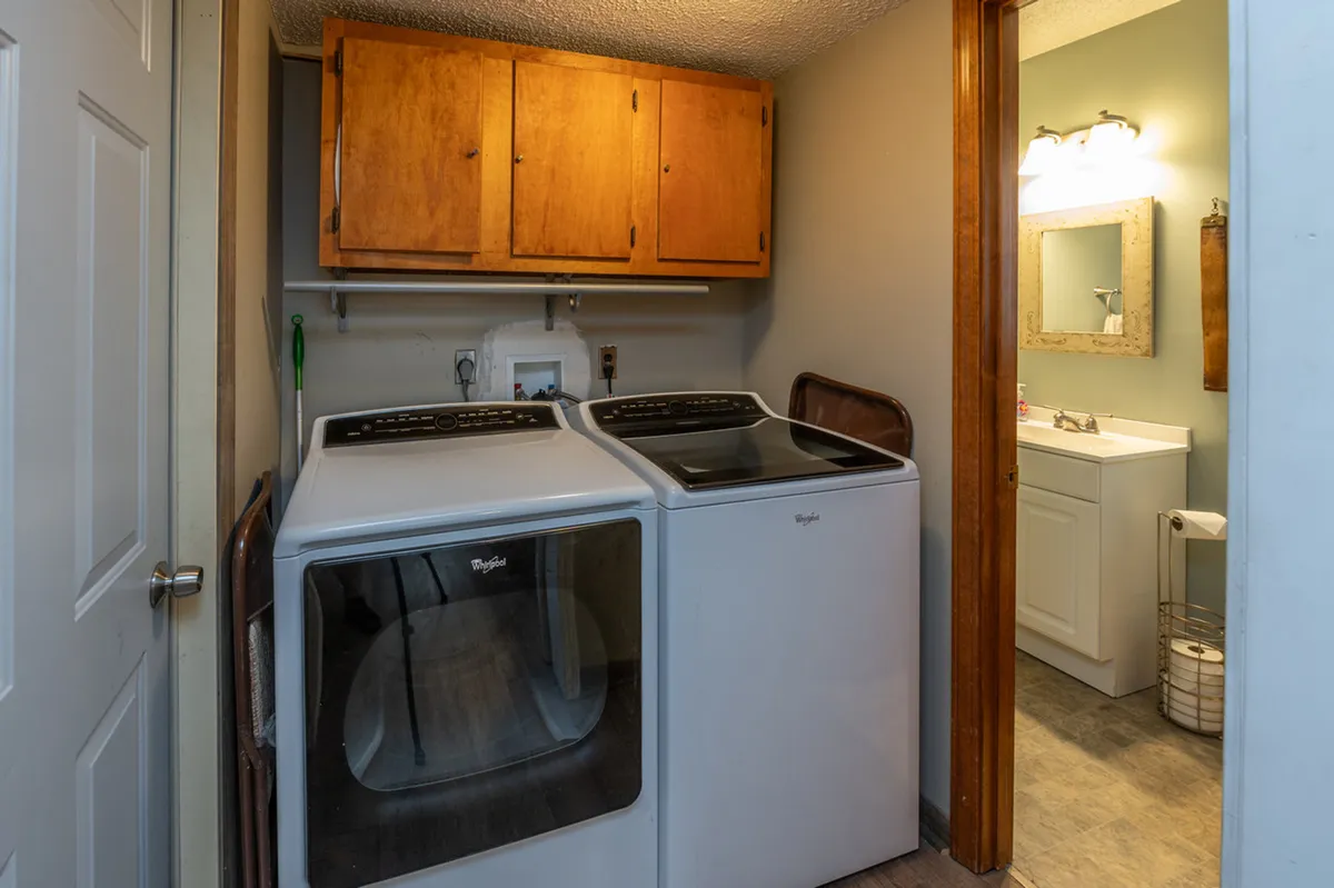 A well-lit, practical room featuring a washing machine, dryer, and a vanity with a mirror. Storage cabinets are visible, demonstrating organized space for household items and gear. The overall mood is cozy yet functional, signaling readiness for outdoor adventures or daily life.