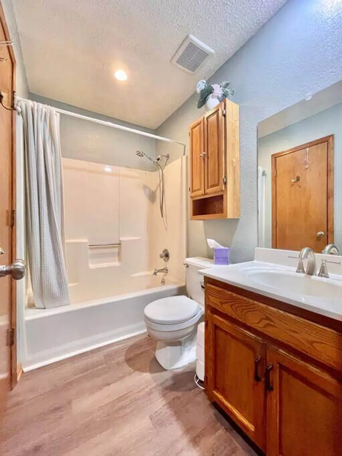 A well-appointed bathroom featuring a bathtub, spacious vanity with mirror, and wooden cabinets. The space is organized, tidy, and filled with natural and artificial light, making it feel both luxurious and practical.