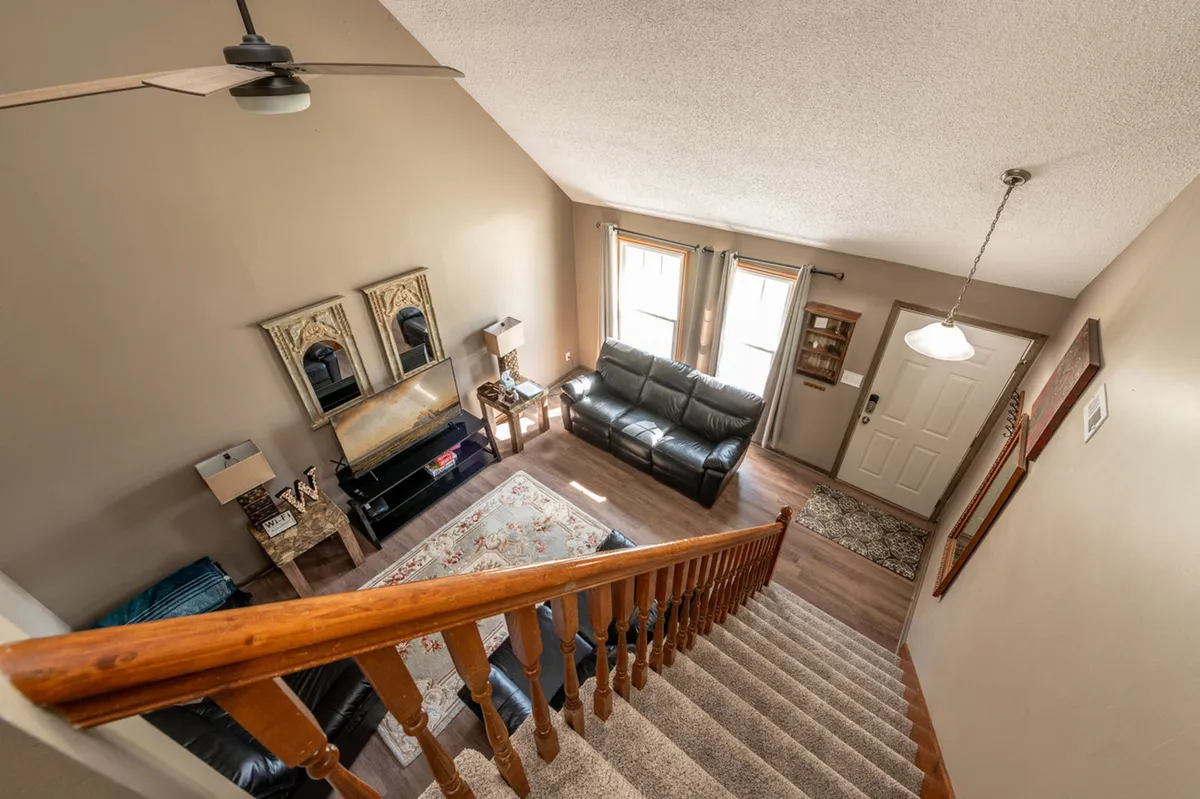 A welcoming living space with a comfortable sofa facing a coffee table, mirrors that reflect natural light, and a front door visible near a staircase—hinting at immediate access to the outside world. Subtle decorative touches and a cozy arrangement convey a relaxing, social atmosphere.